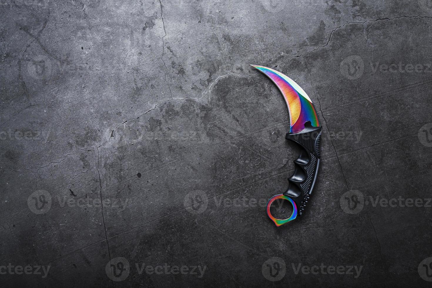 kerambit dolk met een regenboogkleurig blad Aan een donker getextureerde achtergrond. foto