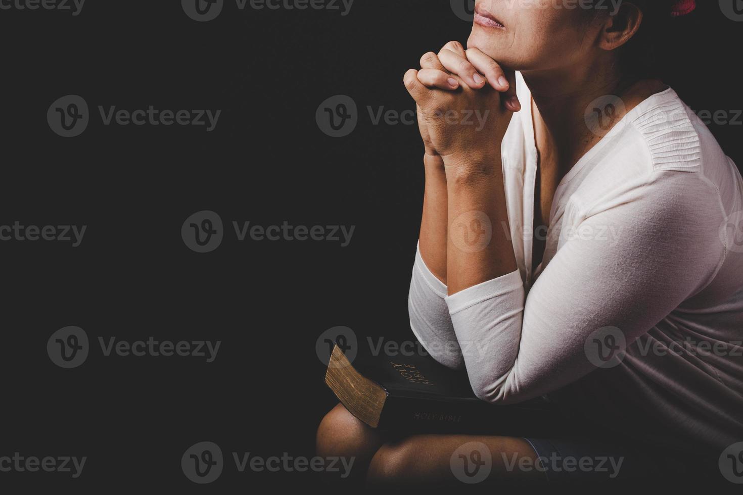 christelijke vrouw hand op heilige bijbel zijn bidden en aanbidden voor god zij dank in de kerk met zwarte achtergrond, concept voor geloof, spiritualiteit en religie foto