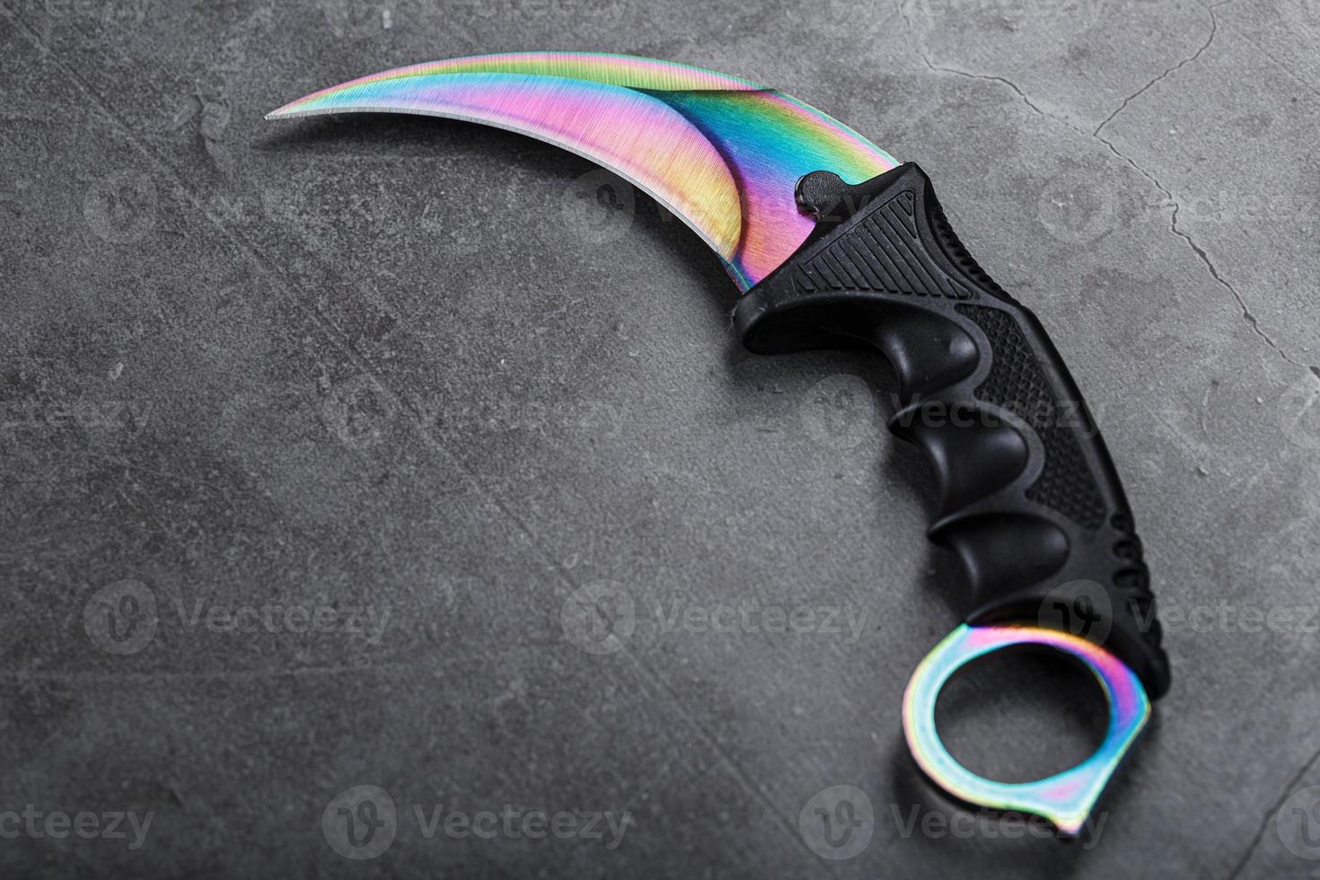 kerambit dolk met een regenboogkleurig blad Aan een donker getextureerde achtergrond. foto