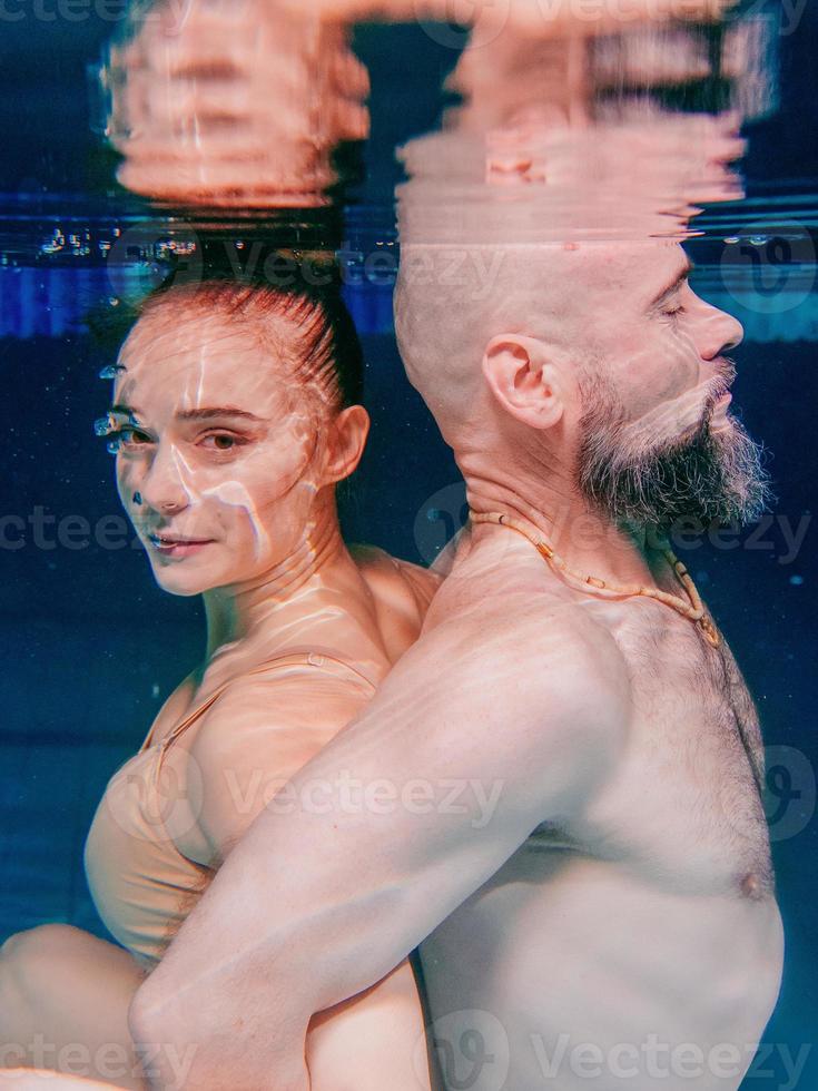 onderwater- portret van de atletisch, sportief dansen en aan het doen yoga asana's paar Mens en vrouw onderwater- in de zwemmen zwembad foto