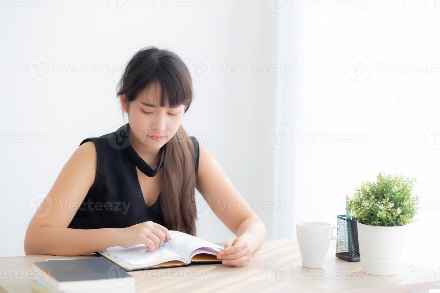 mooie jonge aziatische vrouw glimlachend zittend studeren en leren schrijven notebook en dagboek in de woonkamer thuis, meisje huiswerk, zakenvrouw werken aan tafel, onderwijs concept. foto