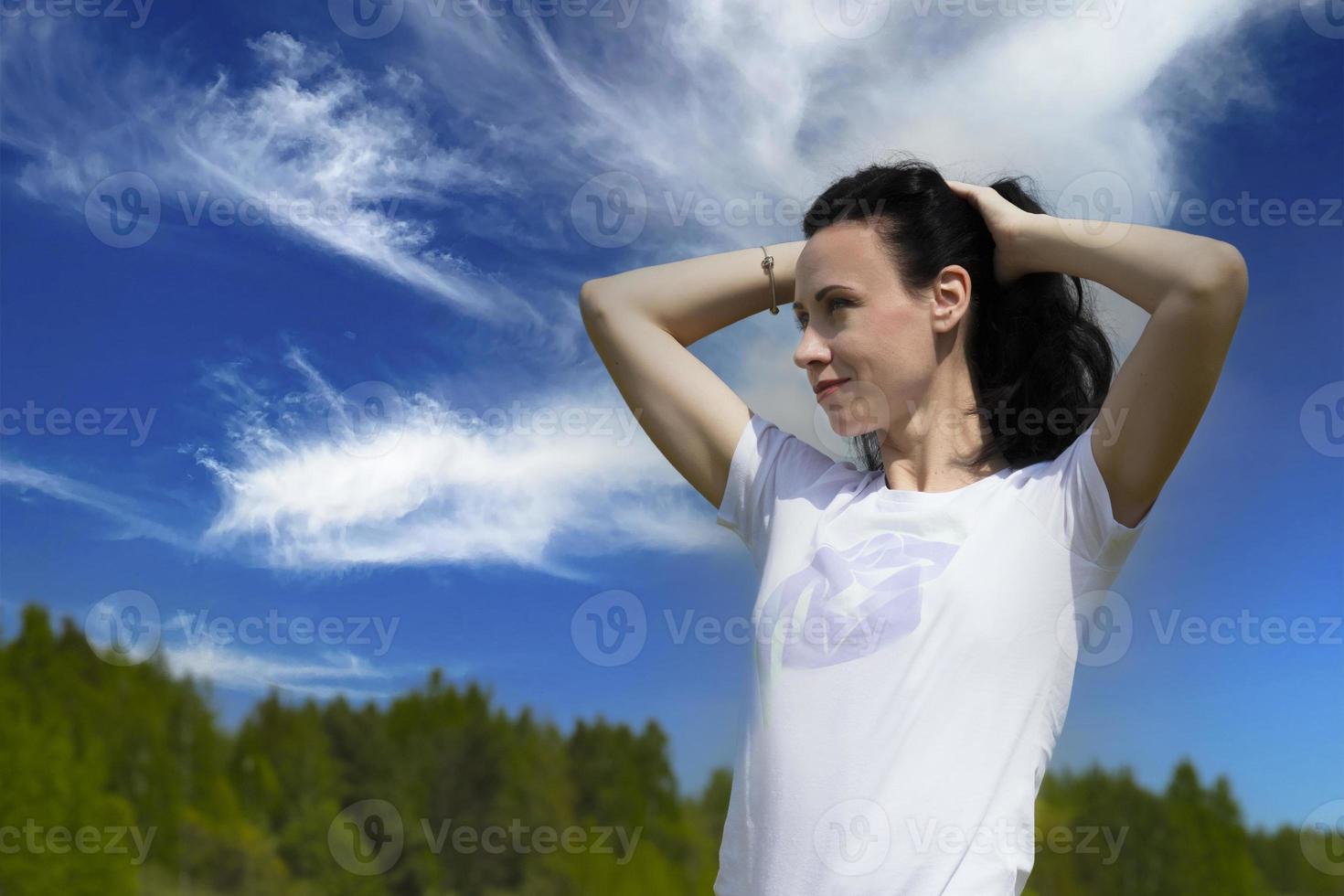 detailopname portret van een mooi jong brunette vrouw met lang haar- tegen een blauw lucht met wolken Aan een zonnig dag, levensstijl, poseren en lachend. kopiëren ruimte. foto