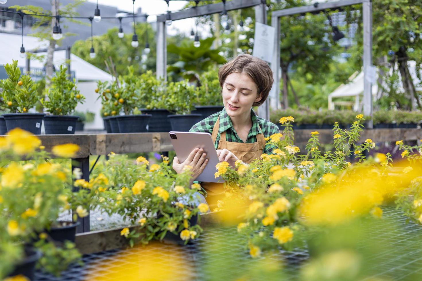 Kaukasisch tuin eigenaar is neigen naar haar sier- bloem fabriek Bij kinderkamer tuin centrum gebruik makend van digitaal tablet voor inheems en exotisch fabriek teler concept foto