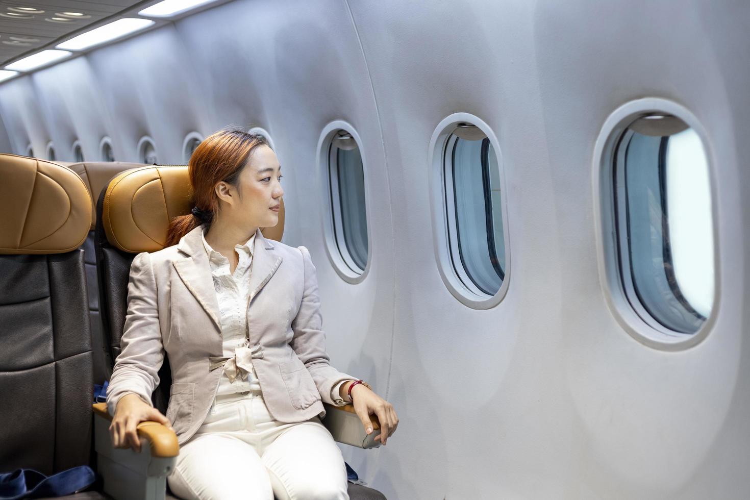Aziatisch vrouw reist zittend comfortabel in de vliegtuig terwijl op zoek uit de venster voor bedrijf reizen in economie klasse stoel foto
