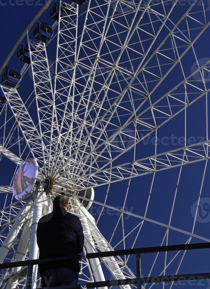 een Mens staat in voorkant van een groot ferris wiel Aan een zonnig dag in dusseldorf, duitsland. foto