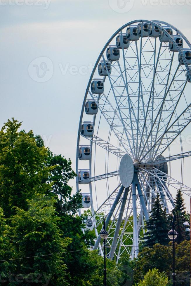 landschap van een pretpark met de top van een reuzenrad dat boven de boomtoppen tegen een blauwe lucht weergeeft. foto