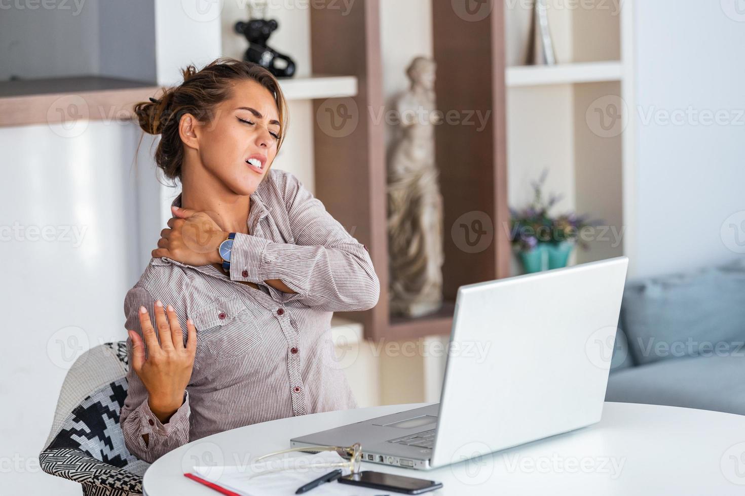 portret van jong benadrukt vrouw zittend Bij huis kantoor bureau in voorkant van laptop, aanraken pijn doen terug met gepijnigd uitdrukking, lijden van rugpijn na werken Aan pc foto