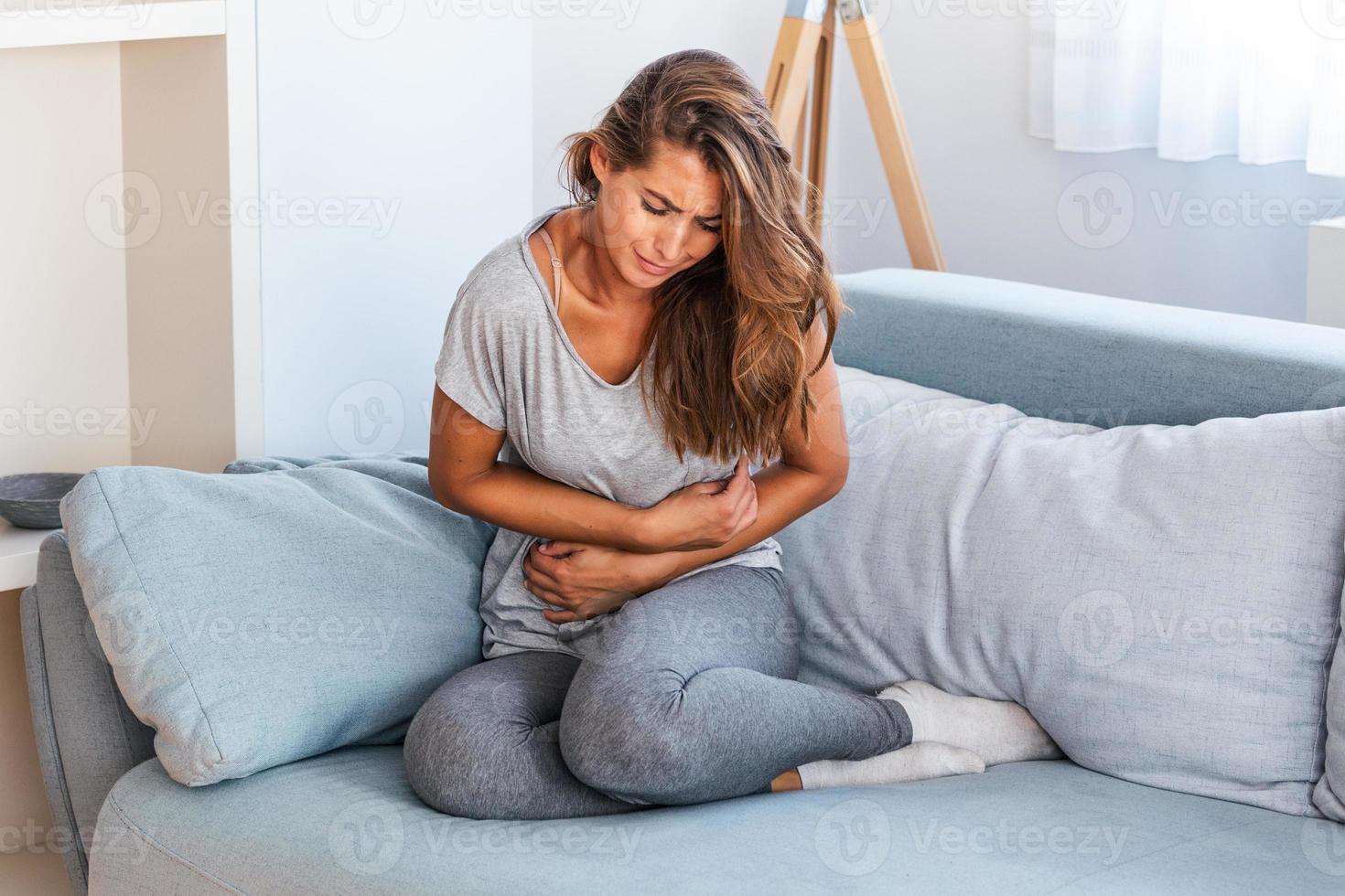 vrouw aan het liegen Aan sofa op zoek ziek in de leven kamer. mooi jong vrouw aan het liegen Aan bed en Holding handen Aan haar maag. vrouw hebben pijnlijk maagpijn Aan bed, menstruatie- periode foto