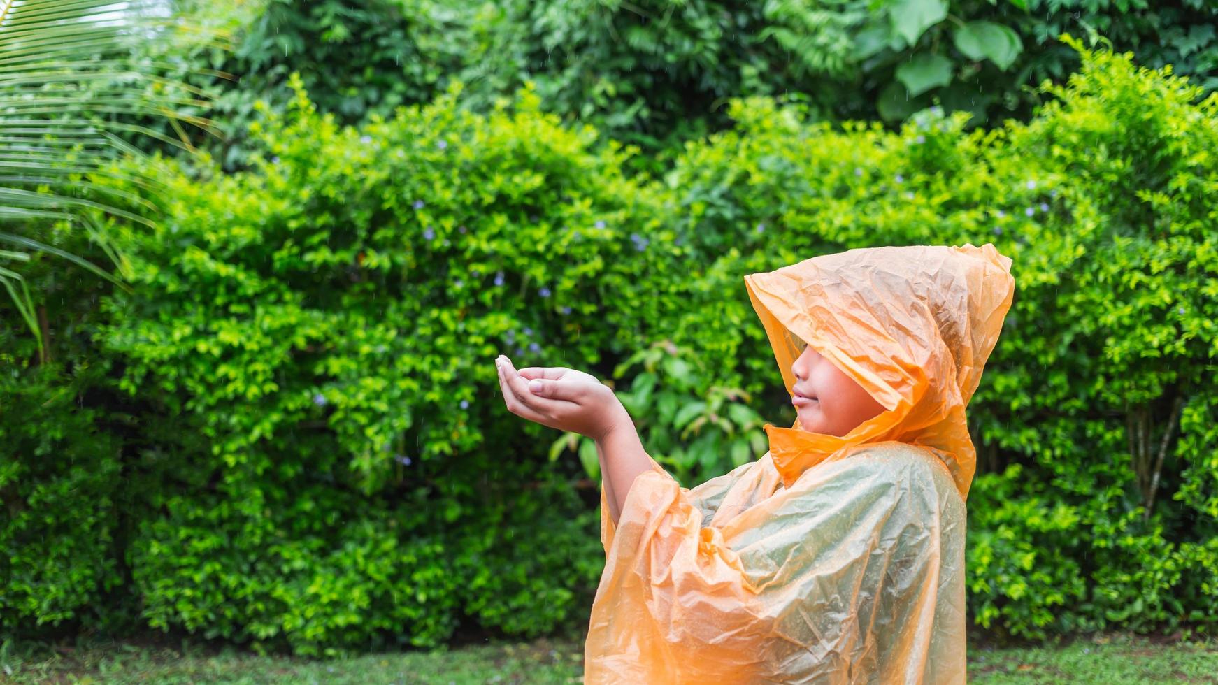 Aziatisch jongen vervelend oranje regenjas is gelukkig en hebben pret in de regen Aan een regenachtig dag. foto