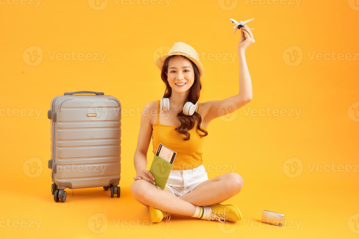 schattig en vrolijk vrouw met een paspoort in de handen van vlak kaartjes in de buurt de grijs koffer foto