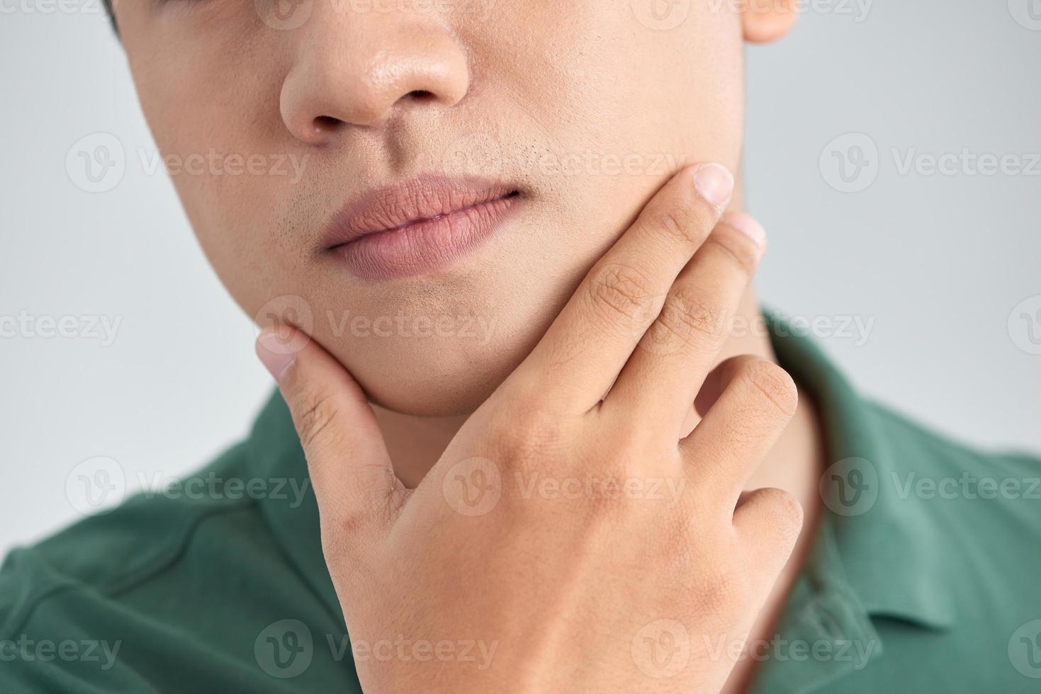 een dichtbij omhoog portret van jong denken Mens aanraken zijn kin met hand- en staand tegen licht grijs achtergrond. denken uit luid foto