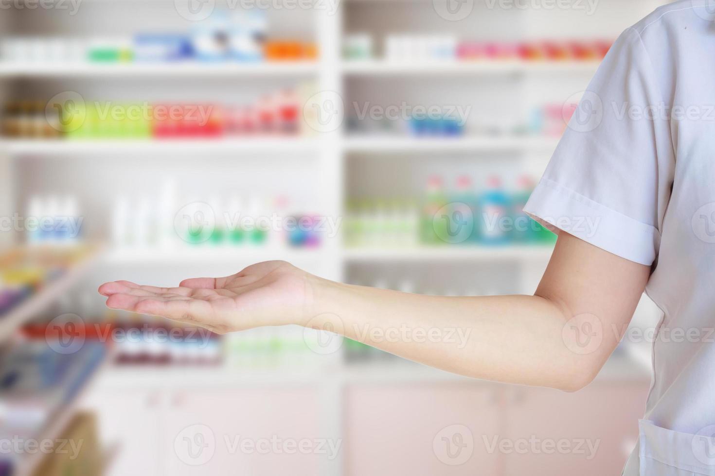 vrouw apotheker met vervagen schappen gevulde met geneesmiddel in de apotheek foto