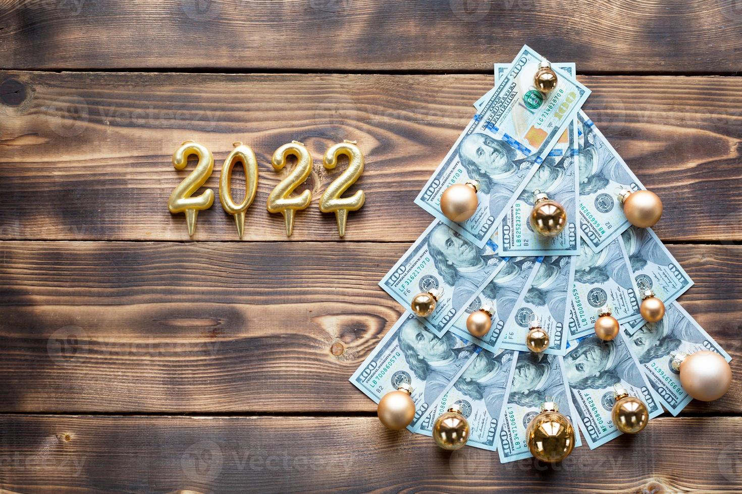 Kerstmis boom gemaakt van 100 dollar rekeningen Aan houten achtergrond met copyspace en 2022. Kerstmis decor van financiën, besparingen, rijkdom, onkosten in nieuw jaar. vlak. stack van 100, investeringen, bedrijf foto