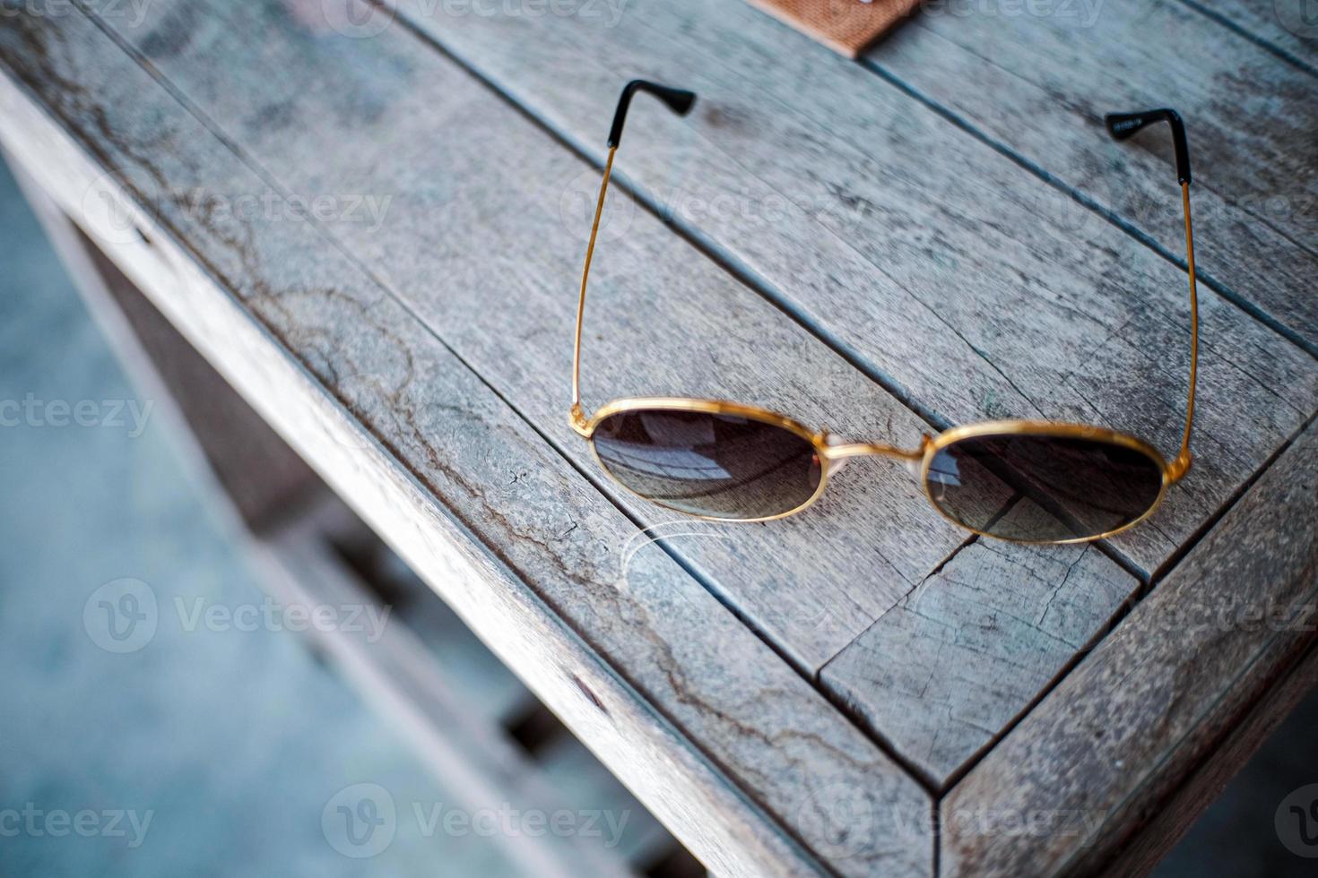 een houten tafel met zonnebril rust tegen een leeg ruimte voor berichten. foto