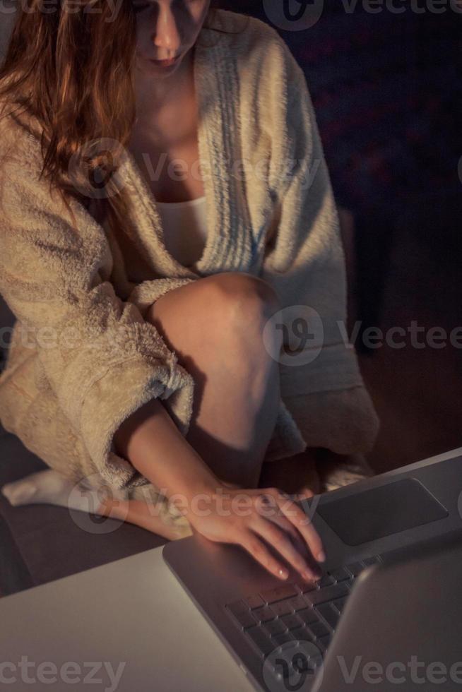 vrouw in badjas gebruik makend van laptop laat Bij nacht. foto