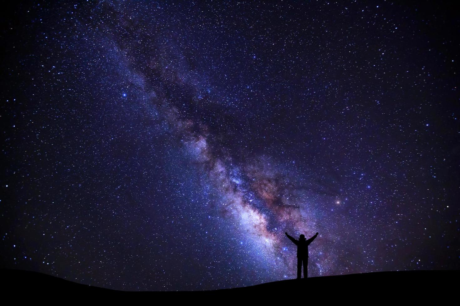 landschap met melkachtig manier, nacht lucht met sterren en silhouet van een staand sportief Mens met verheven omhoog armen Aan hoog berg. foto