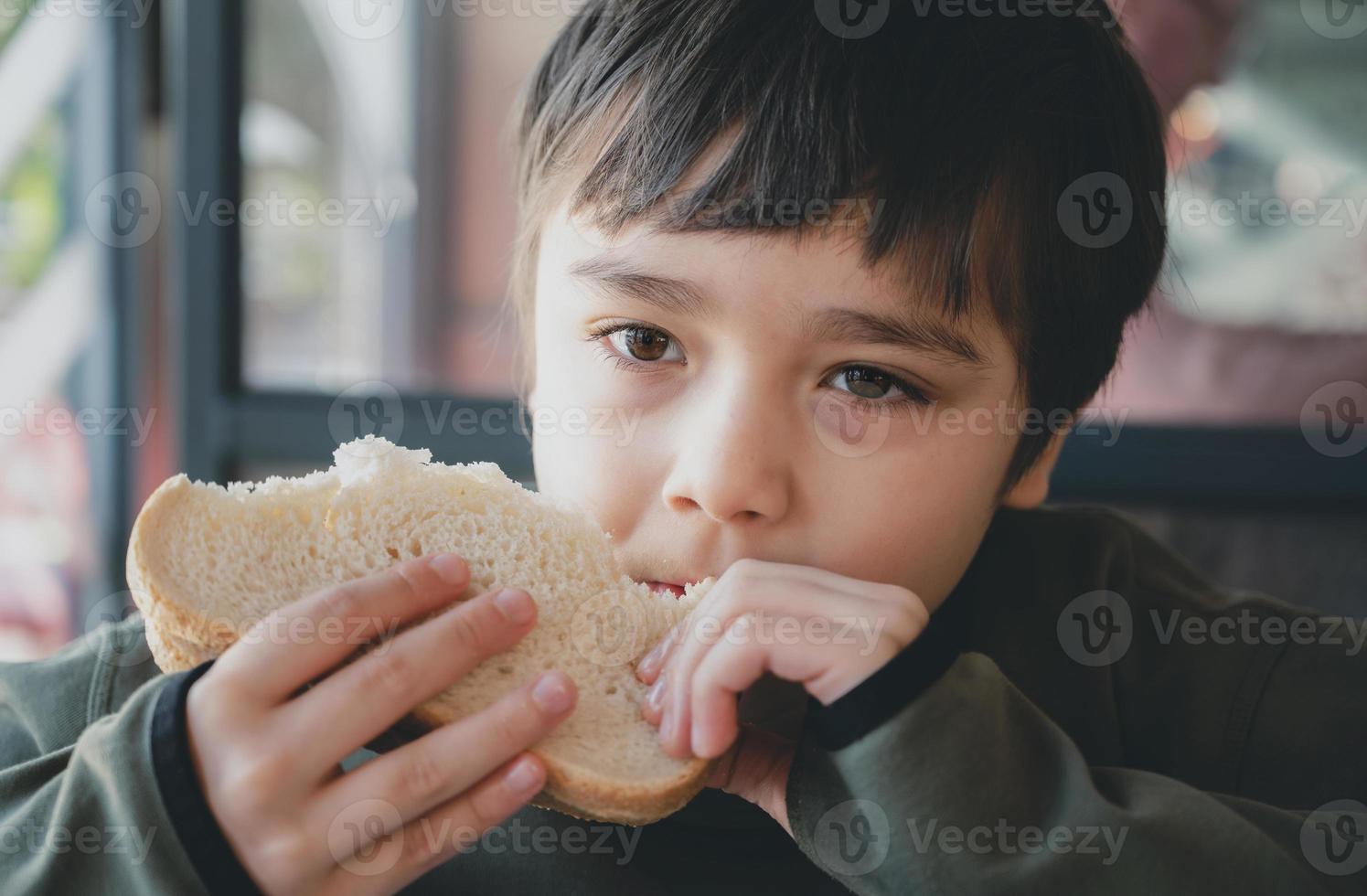 portret gezond jong jongen aan het eten spek broodje, school- kind hebben ontbijt in de cafe worden voor Gaan naar school, kind bijten geroosterd brood belegd broodje rundvlees Cheddar kaas voor lunch. foto