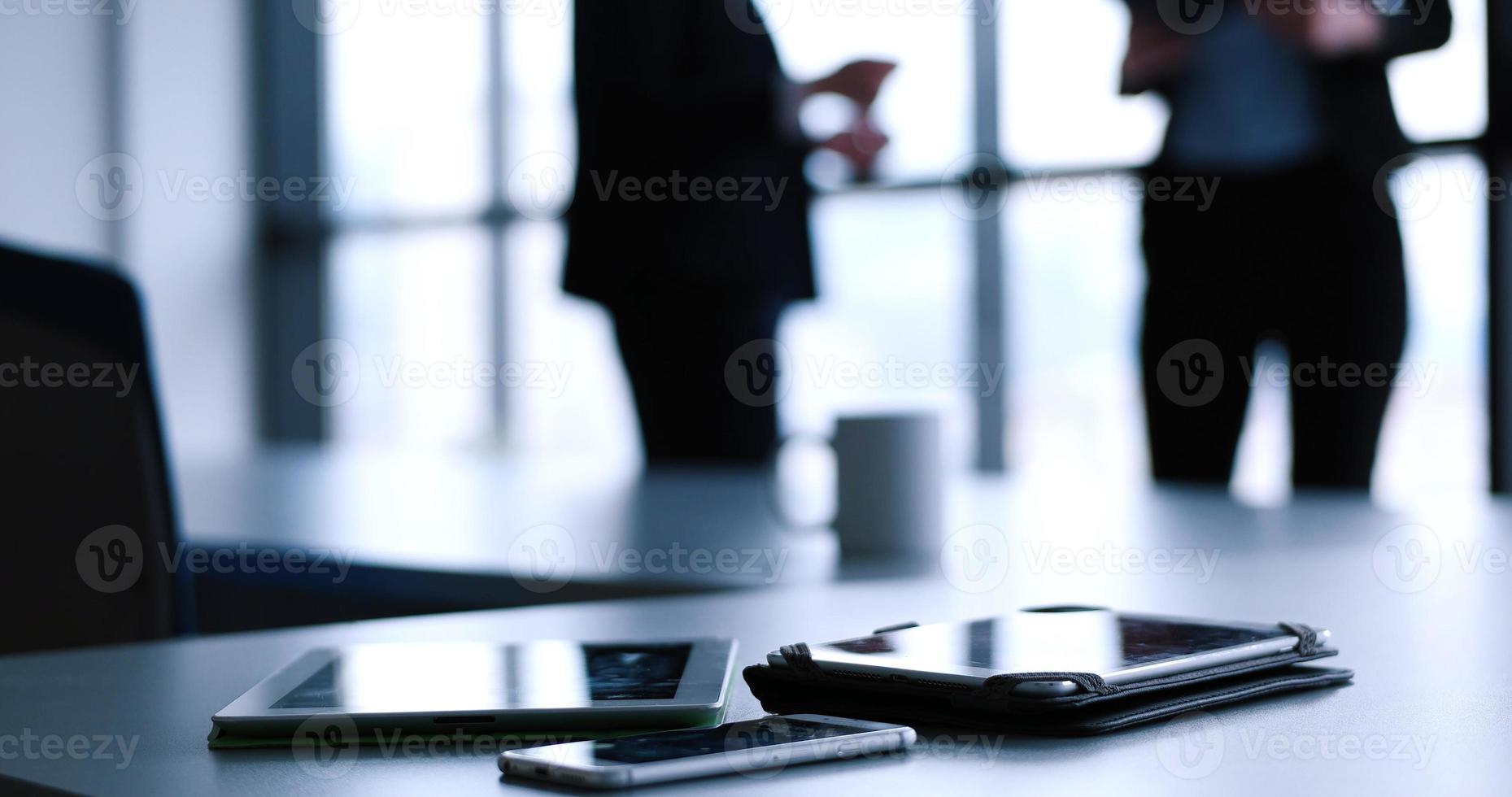 tablet, mobiel cel telefoon en kop van koffie in kantoor met bedrijf mensen in backgorund foto