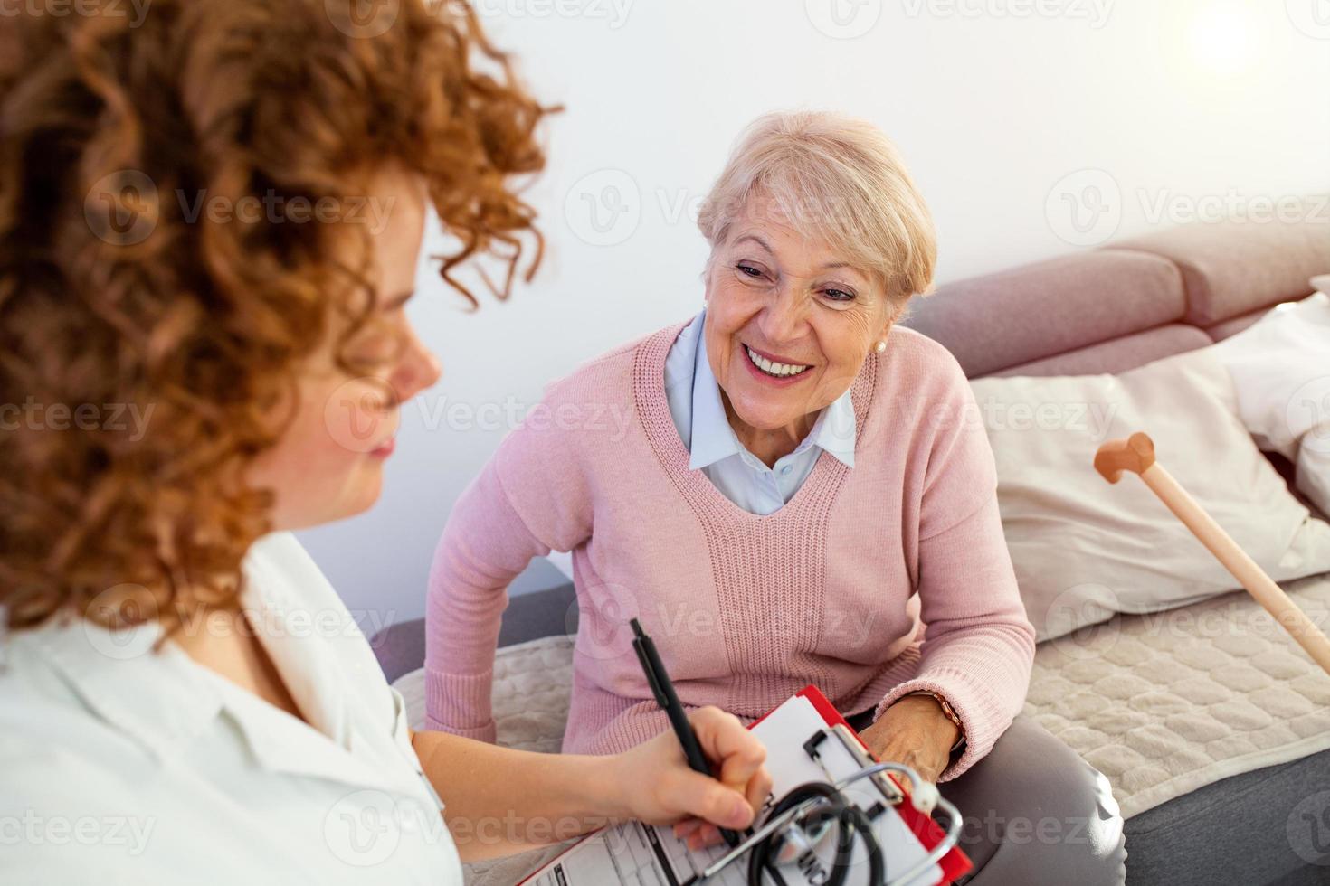 senior vrouw is bezocht door haar dokter of verzorger. vrouw dokter of verpleegster pratend met senior geduldig. geneesmiddel, leeftijd, Gezondheid zorg en huis zorg concept. senior vrouw met haar verzorger Bij huis foto