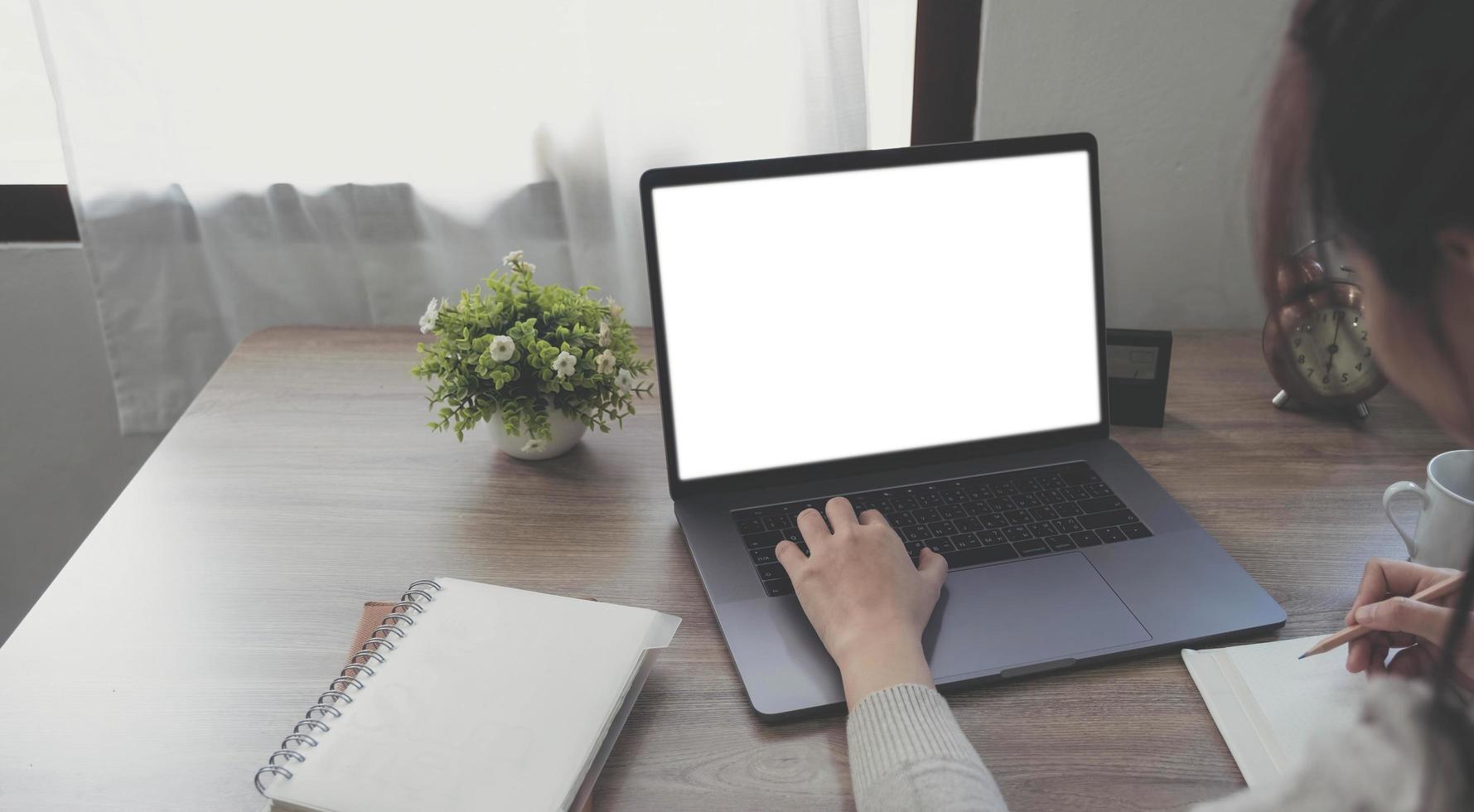 mockup beeld van een vrouw gebruik makend van en typen Aan laptop met blanco wit bureaublad scherm Aan houten tafel foto