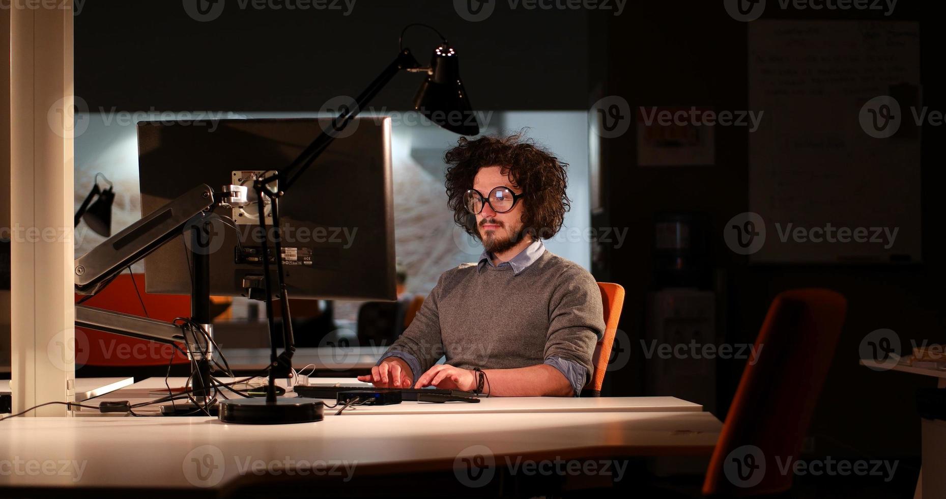 Mens werken Aan computer in donker kantoor foto