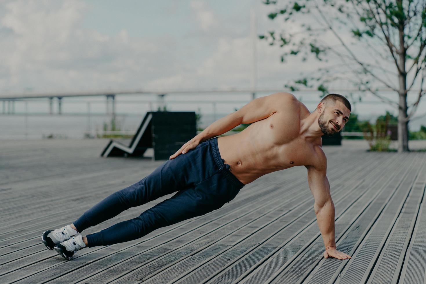 sportief bodybuilder staat in kant plank, opdrachten buitenshuis en draagt sport kleren, Leidt gezond levensstijl, heeft fit lichaam en spieren. buitenshuis schot van vastbesloten sportman doet Gezondheid activiteiten foto