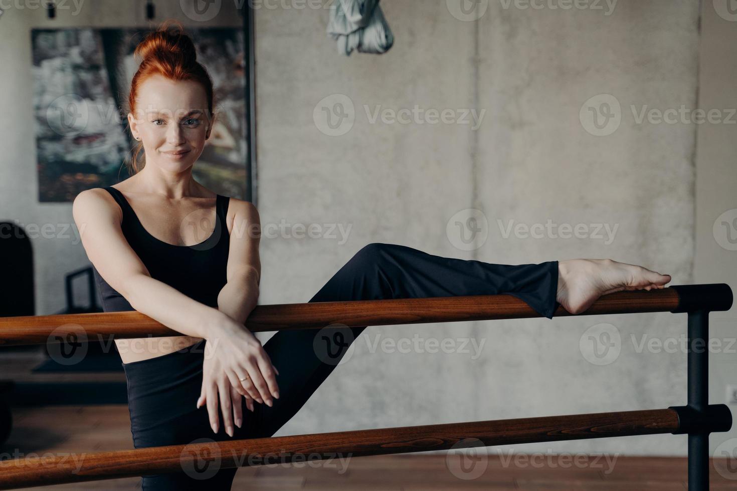 atletische glimlachende gembervrouw die geniet van stretching training op ballet barre foto