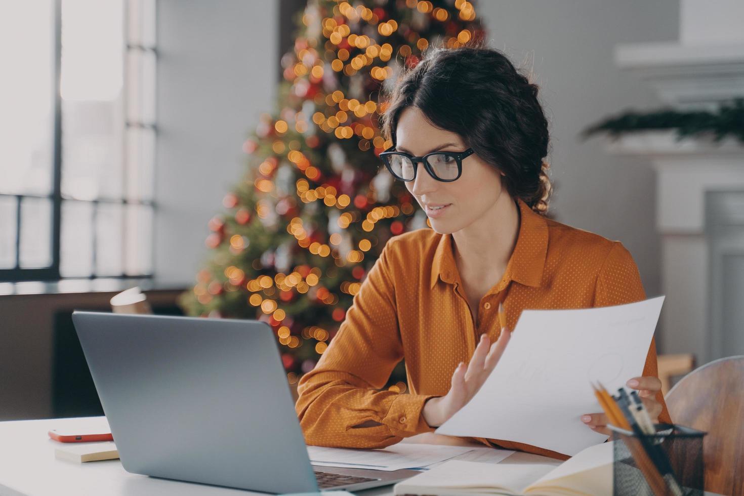 Spaanse zakenvrouw met een bril die met kerst online op kantoor werkt foto