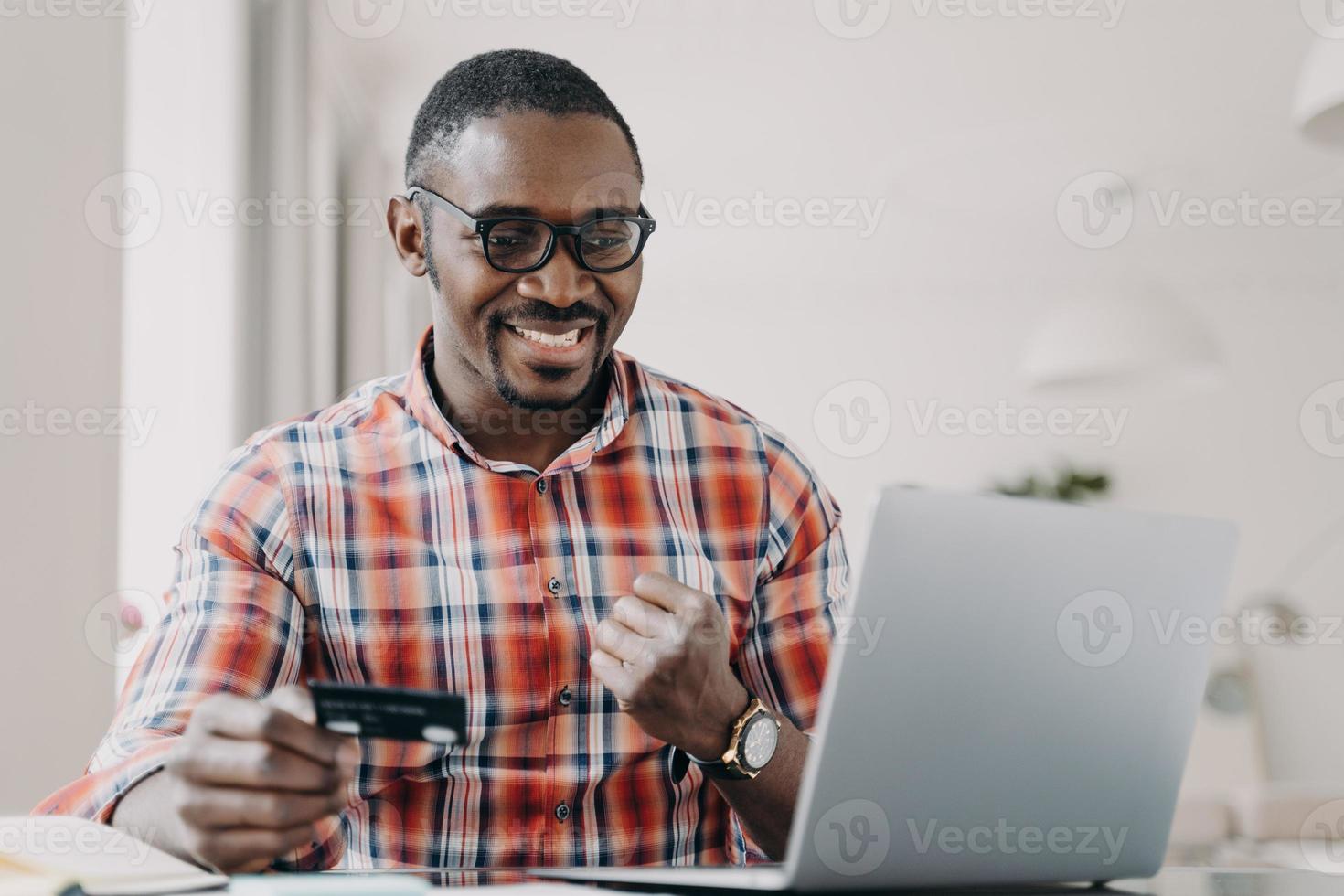 e-banking, e-commerce. Afro-Amerikaanse man met creditcard gebruikt e-bank online service op laptop foto