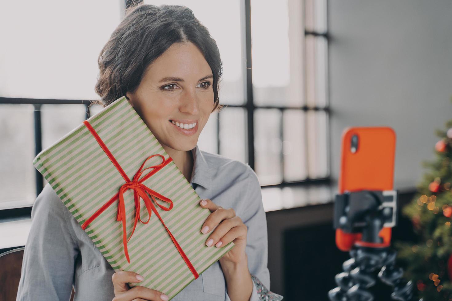 lachende vrouwelijke blogger die tijdens de kerstvakantie live online streamt via mobiele telefoon op statief foto