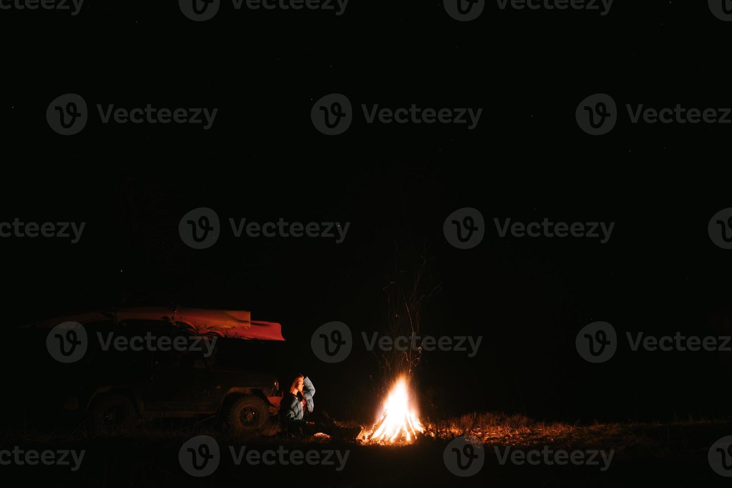 vrouw zittend en krijgen warm in de buurt de vreugdevuur in de nacht Woud. foto