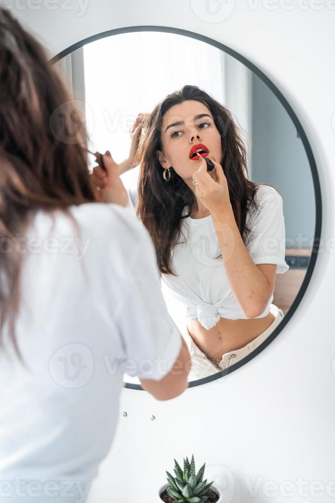 jong vrouw toepassen lippenstift op zoek Bij spiegel foto