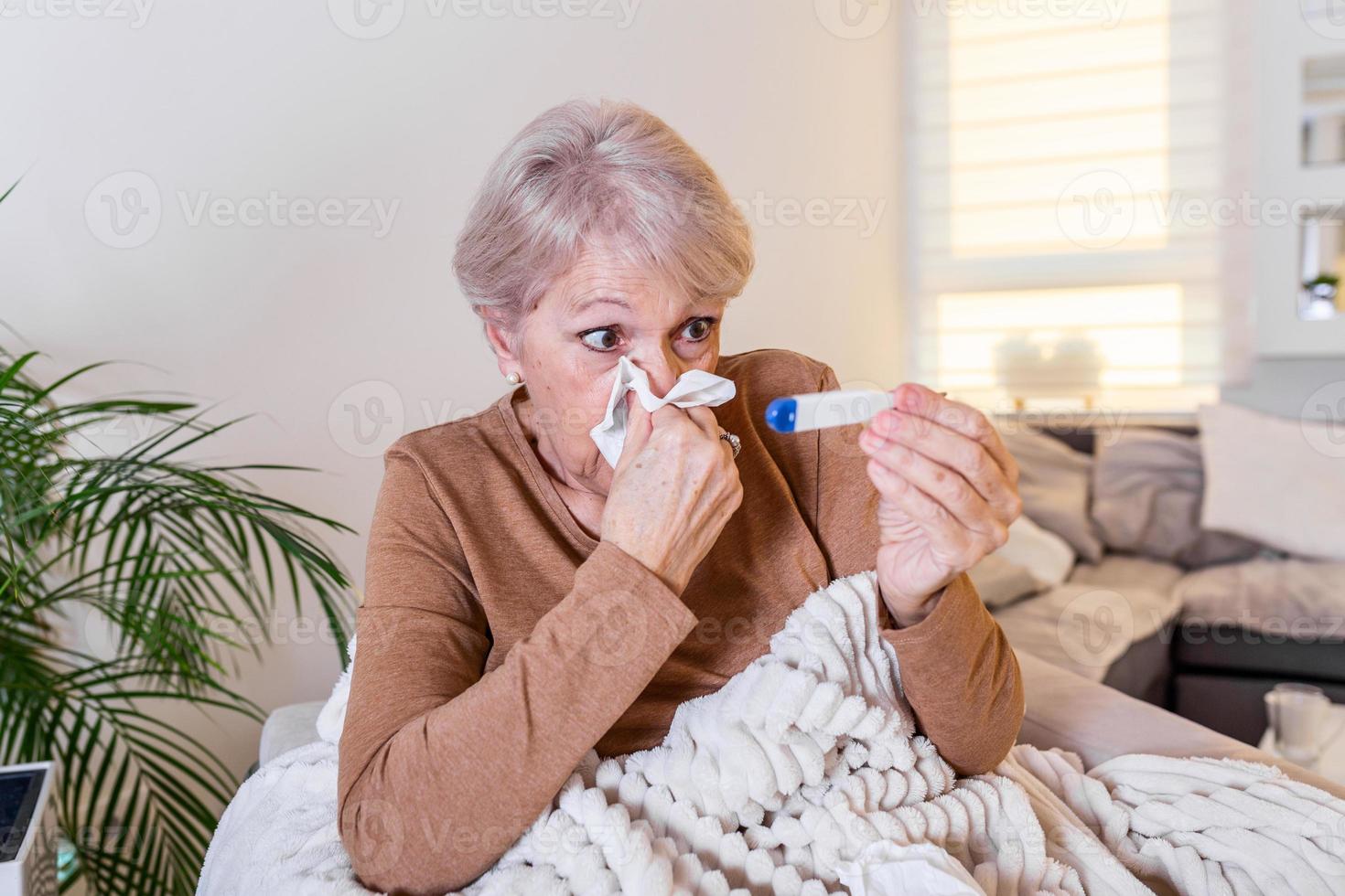 ziekte, coronavirus probleem concept. senior vrouw wezen ziek hebben griep aan het liegen Aan sofa op zoek Bij temperatuur Aan thermometer. covid19 pandemisch foto