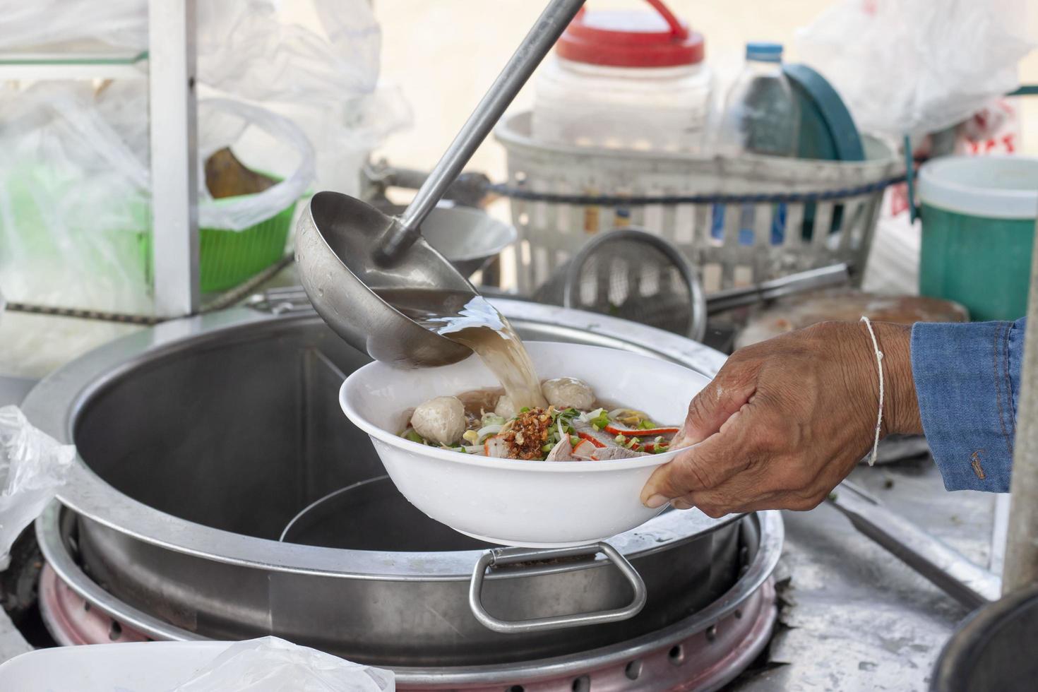 hand- van Aziatisch chef Koken noodle soep met vlees bal in lokaal restaurant, Thailand straat voedsel. foto