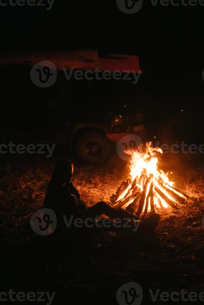 vrouw zittend en krijgen warm in de buurt de vreugdevuur in de nacht Woud. foto