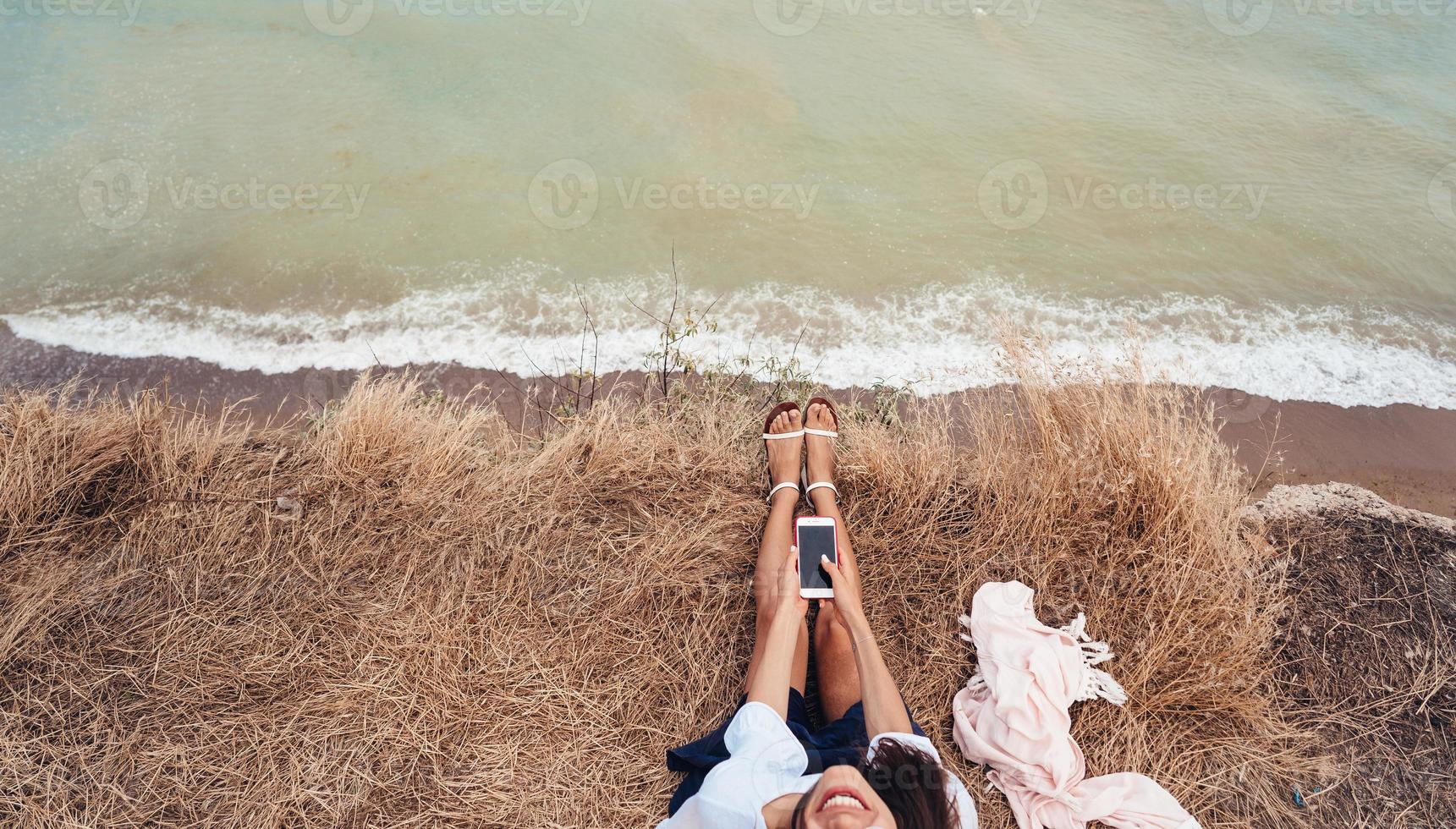 mooi jong meisje zittend en Holding een smartphone in haar handen, top visie foto
