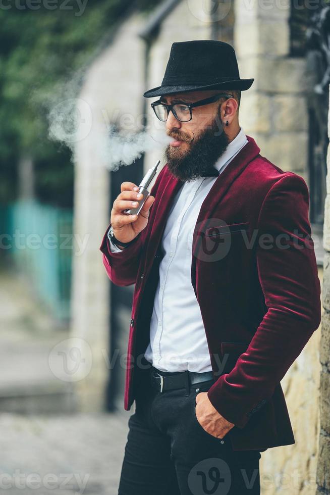een rijk Mens met een baard rookt elektronisch sigaret foto