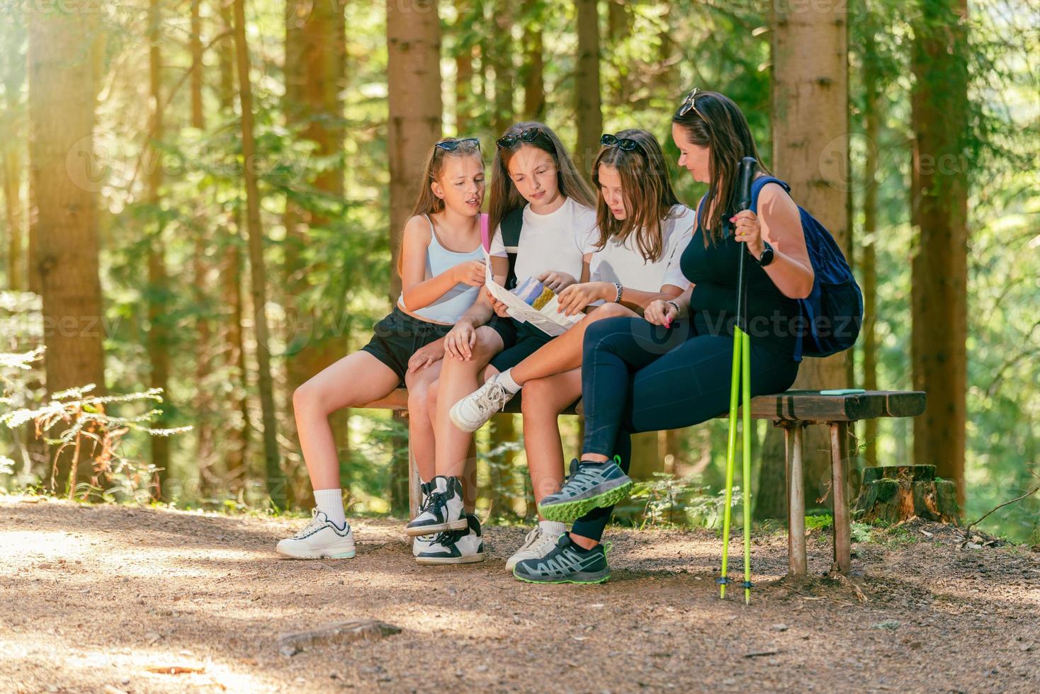 vrouw wandelaars zitten Aan een houten bank in een Woud pad en lezen een kaart van wandelen trails foto