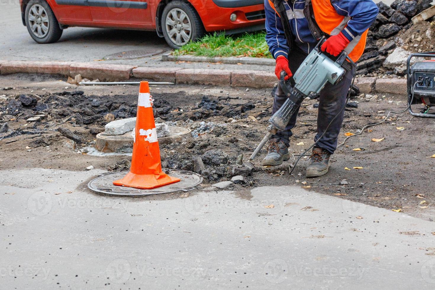 een arbeider gebruik makend van een elektrisch drilboor en een benzine generator reinigt de Oppervlakte in de buurt de riool mangaten van de oud asfalt. foto