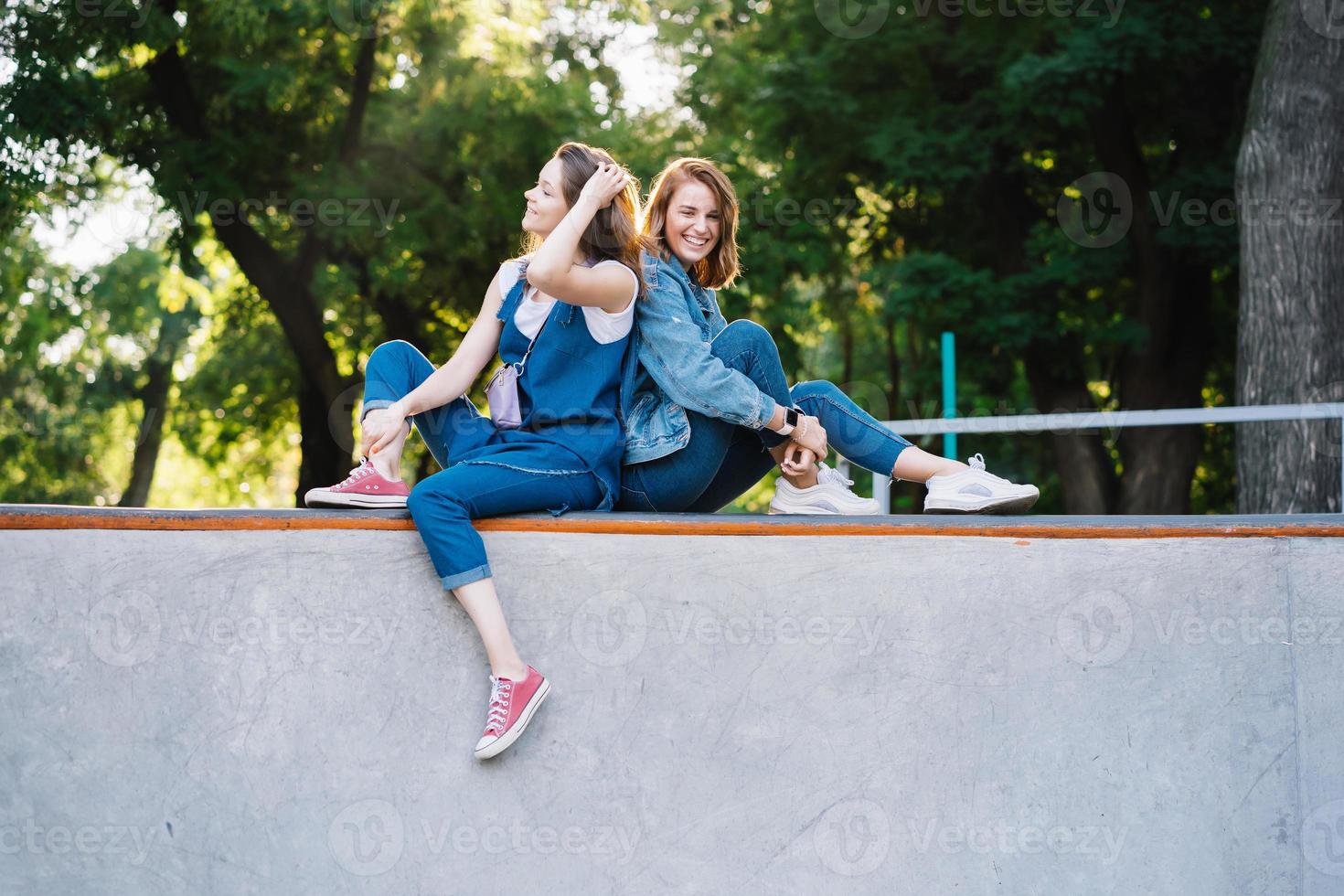 twee gelukkig jong meisjes zittend Bij de vleet park foto