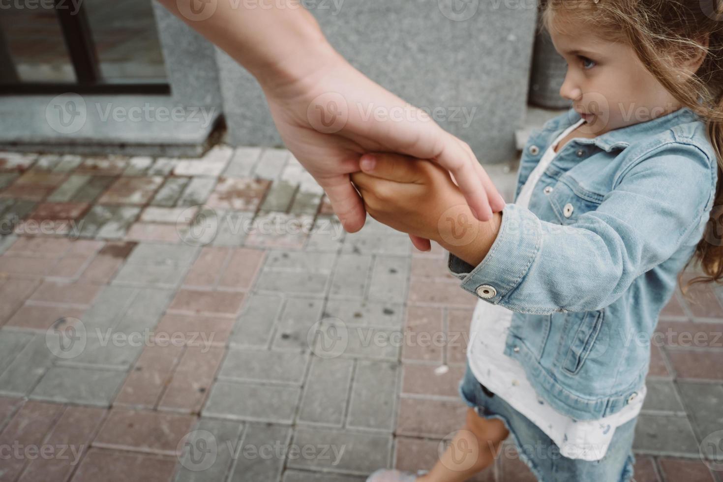 jong moeder en schattig weinig dochter wandelen naar beneden de straat foto