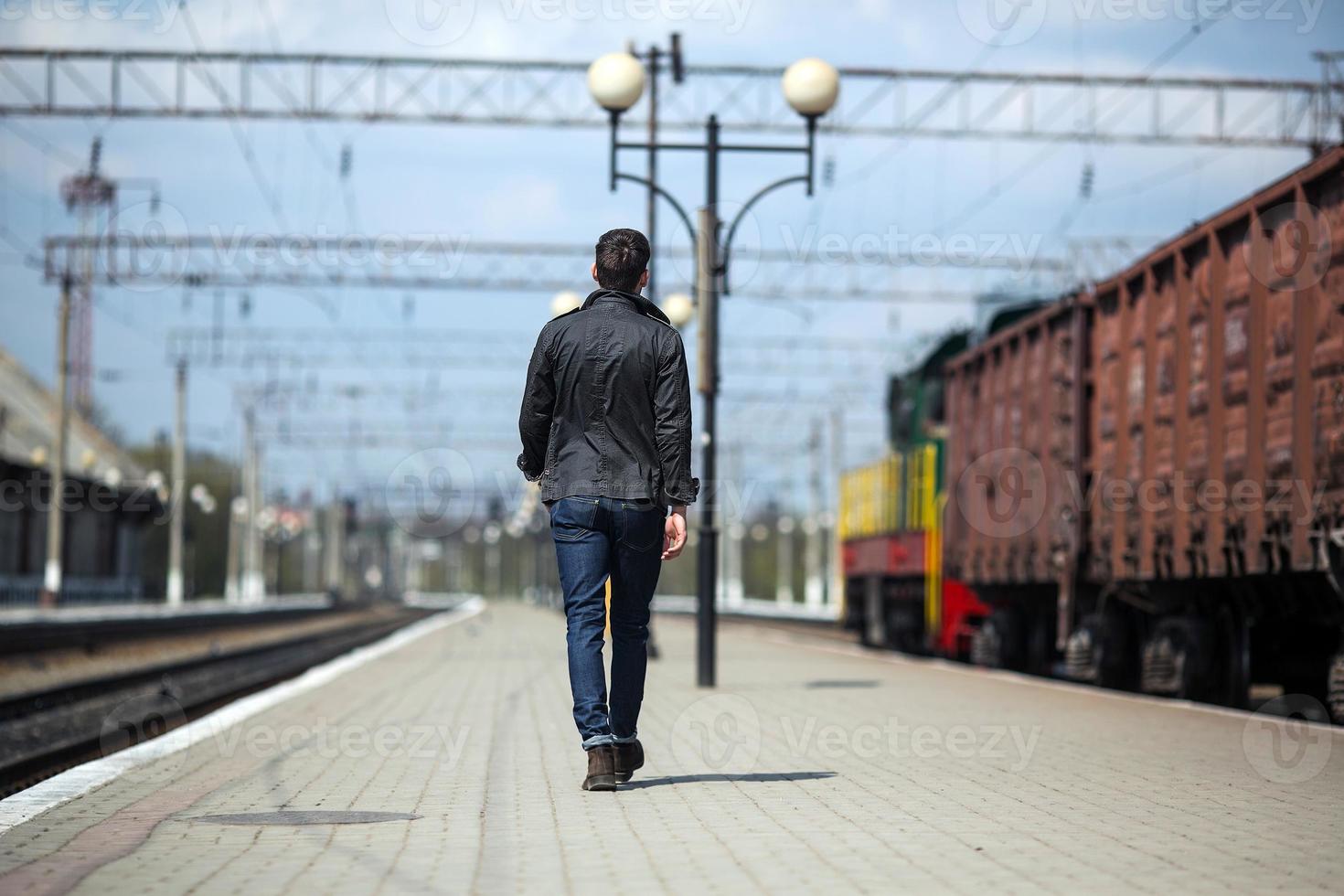 een Mens gekleed in jeans Aan de achtergrond van de trein en de station foto