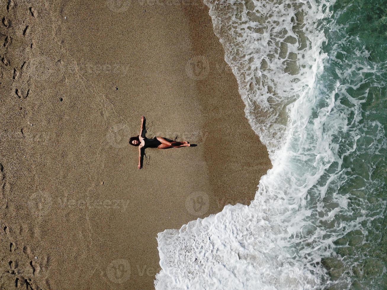 antenne top visie jong vrouw aan het liegen Aan de zand strand en golven foto