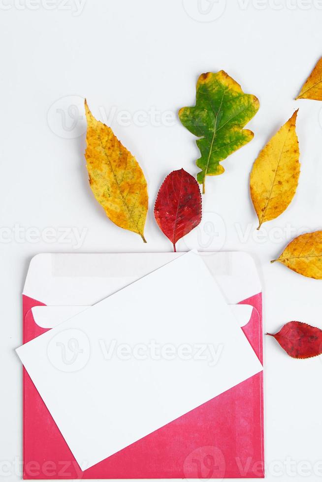 herfst plat leggen. envelop met een lege wenskaart en gevallen gele bladeren op een witte achtergrond. foto