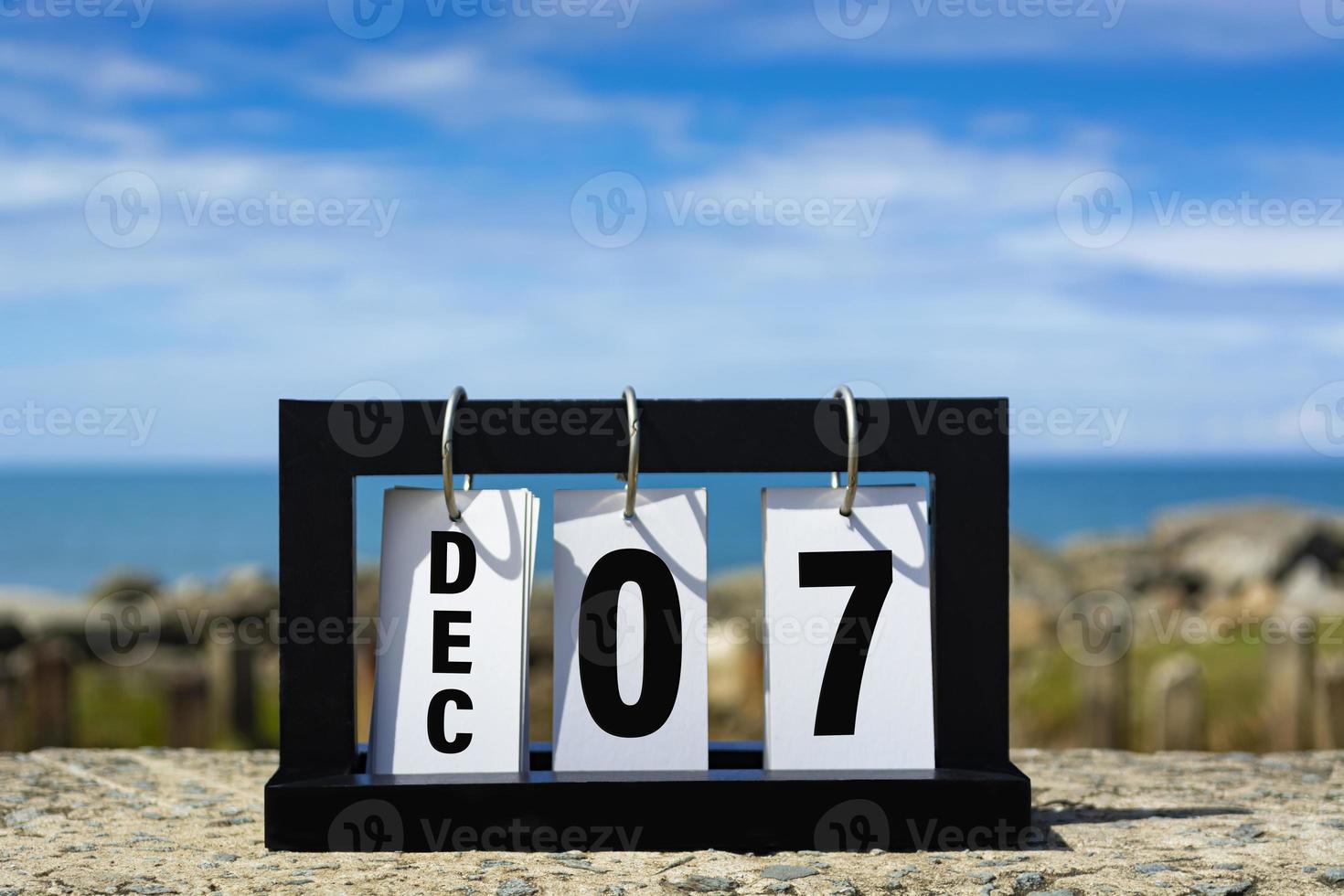 dec 07 kalender datum tekst Aan houten kader met wazig achtergrond van oceaan. foto