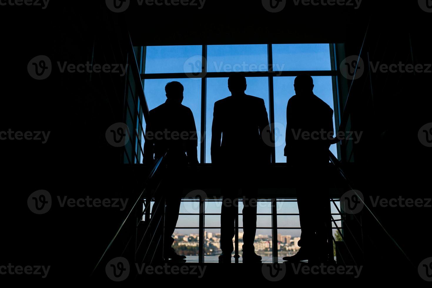 drie zakenlieden staand Bij de venster met een stad visie foto