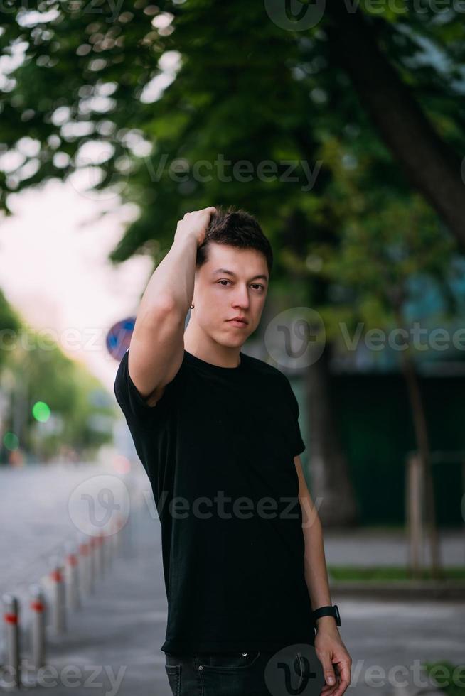 jong volwassen Mens in een zwart t-shirt en jeans wandelingen Aan een stad straat foto