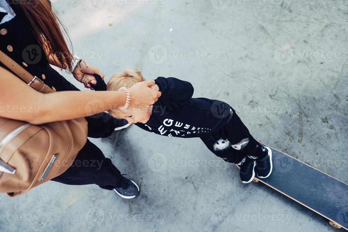 jong moeder geeft les haar weinig jongen naar rijden een skateboard foto