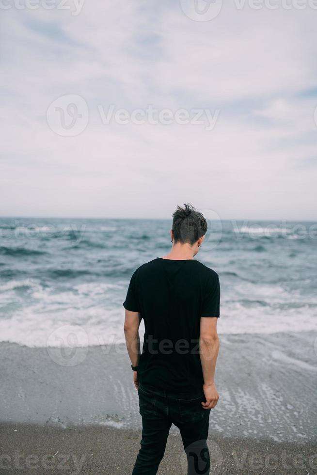 glimlachen vent in een zwart t-shirt staat Aan de zanderig kust. foto