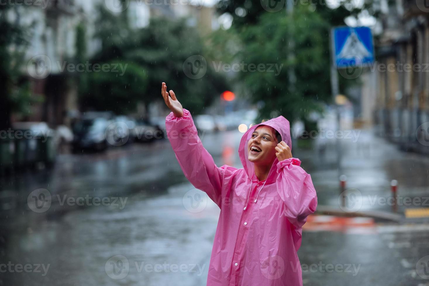 jong glimlachen vrouw met regenjas terwijl genieten van een regenachtig dag. foto